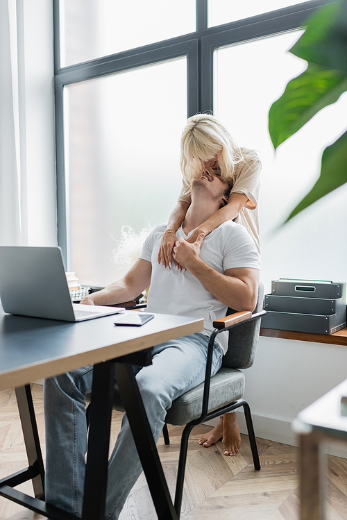 happy woman hugging smiling boyfriend sitting at desk while working from home