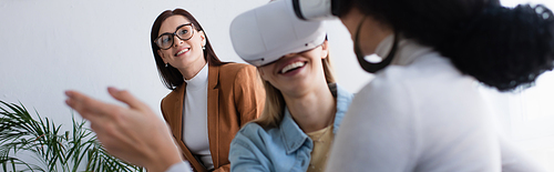 psychologist in eyeglasses smiling near interracial lesbian couple gaming in vr headsets, banner