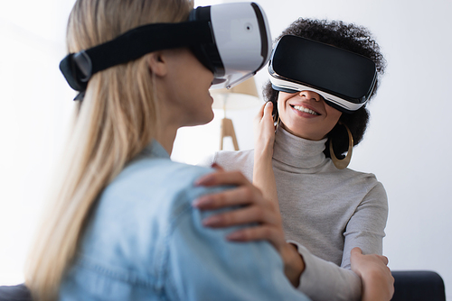 smiling african american women and her blurred lesbian girlfriend gaming in vr headsets at home