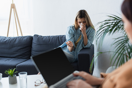 depressed woman crying on couch near blurred psychologist with laptop