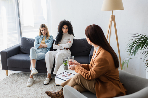 psychologist talking to interracial lesbians sitting on couch with crossed arms