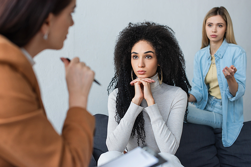 upset couple of interracial lesbians listening to blurred psychologist during consultation