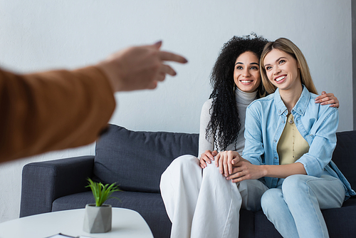 blurred psychologist pointing at multiethnic lesbian women sitting on couch in consulting room
