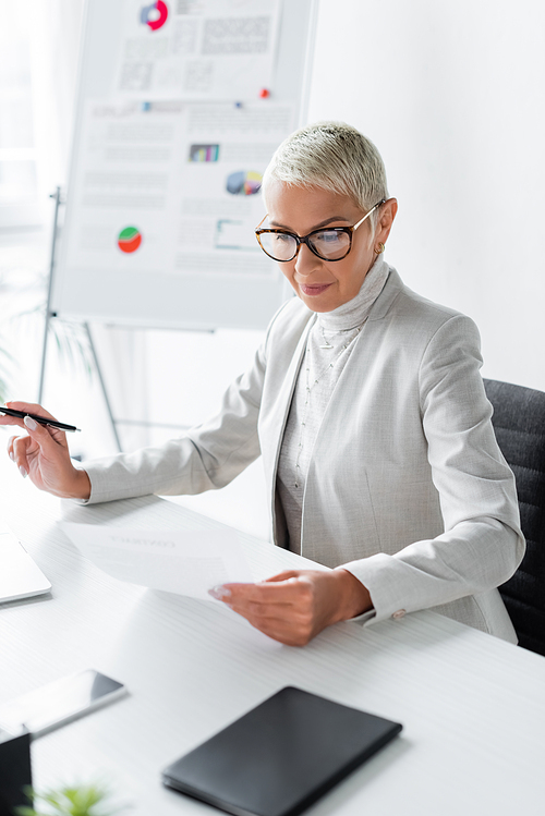 senior businesswoman in glasses looking at document in office