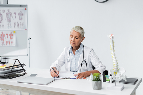 doctor with grey hair writing prescription near devices on desk