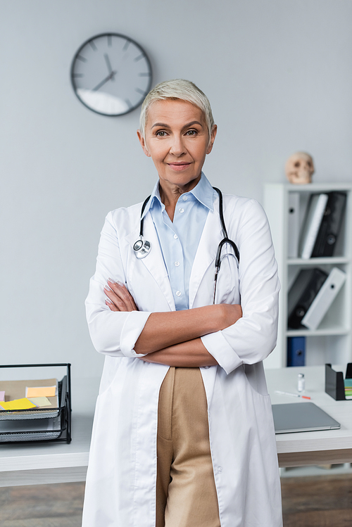 pleased doctor with grey hair in white coat standing with crossed arms