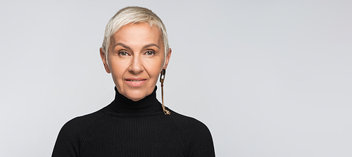smiling senior woman with long earring and black turtleneck  isolated on grey, banner