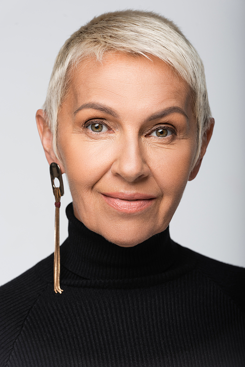 cheerful senior woman with long earring and black turtleneck isolated on grey