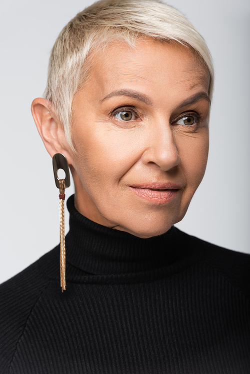 pleased senior woman with long earring and black turtleneck isolated on grey