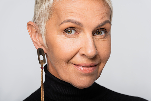 positive senior woman with long earring and black turtleneck isolated on grey