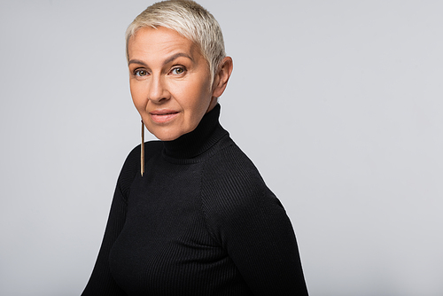 smiling senior woman with long earring and black turtleneck  isolated on grey