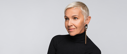 smiling senior woman with long earring and black turtleneck isolated on grey, banner