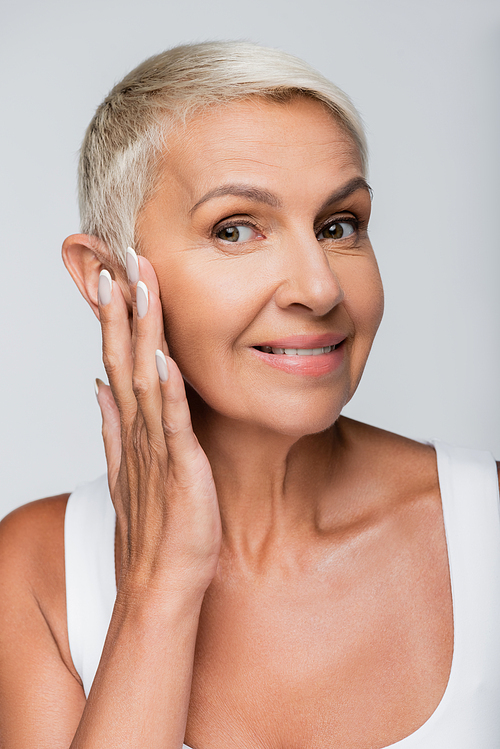 happy senior woman smiling while applying face cream isolated on grey