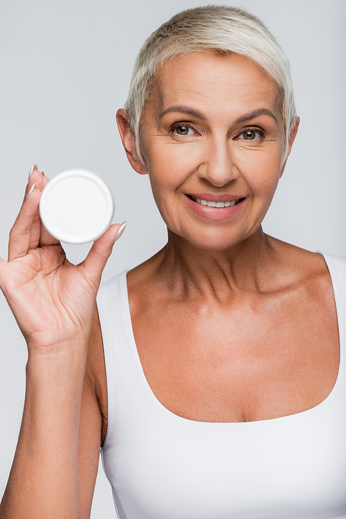 happy senior woman holding container with face cream isolated on grey