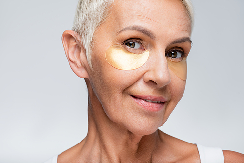smiling senior woman with collagen eye patches isolated on grey