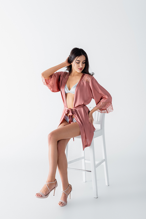 young woman in sexy underwear and satin robe sitting on chair on white