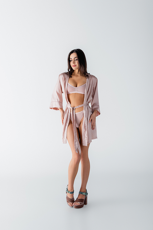 full length of young woman posing in underwear and silk robe on white