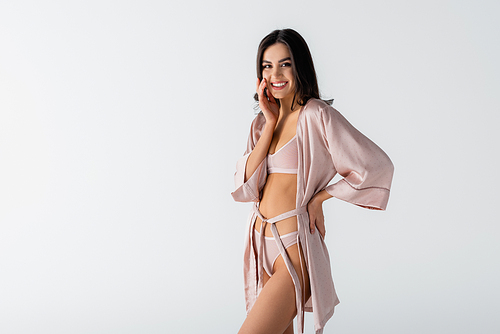 smiling young woman in underwear and silk robe standing with hand on hip isolated on white