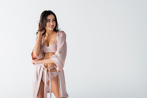 happy young woman in underwear and silk robe looking away isolated on white