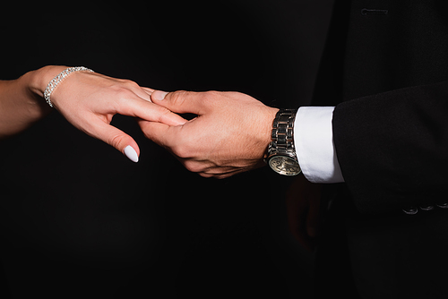 cropped view of man in wristwatch holding hand of woman in bracelet isolated on black