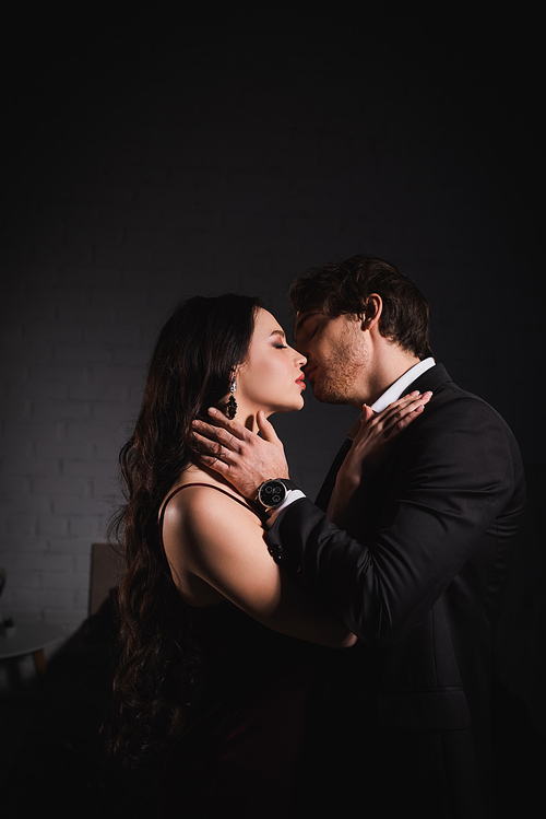 passionate couple in elegant clothes kissing at night in bedroom