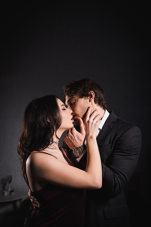 man in suit and sensual woman in elegant dress kissing with closed eyes at night