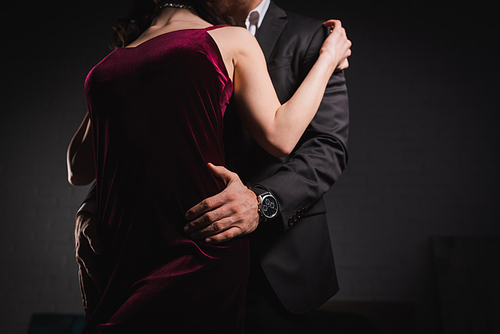 partial view of man in suit embracing hips of elegant woman at night