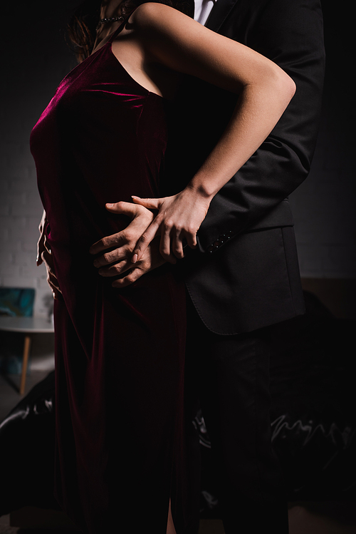 partial view of man seducing woman in elegant dress while hugging her hips at night in bedroom