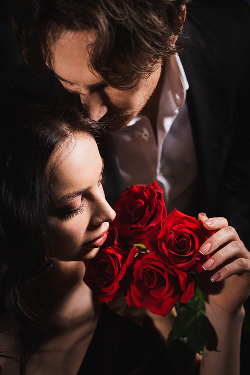 close up view of sensual woman holding red rosed near young man in black suit
