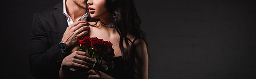 cropped view of man touching shoulder of woman with red roses on dark background, banner