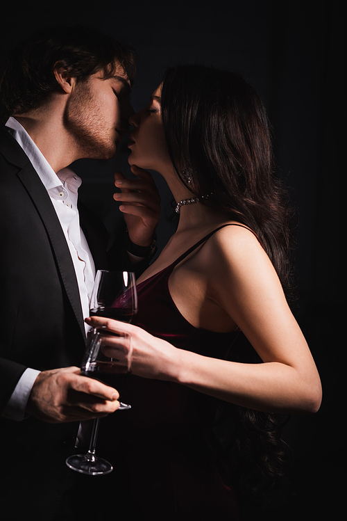 young elegant couple holding wine glasses while kissing with closed eyes at night