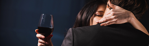 brunette woman with glass of red wine hugging man on dark background, banner