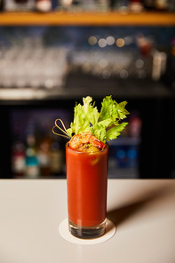 bloody mary cocktail with celery and shrimp in glass on bar counter