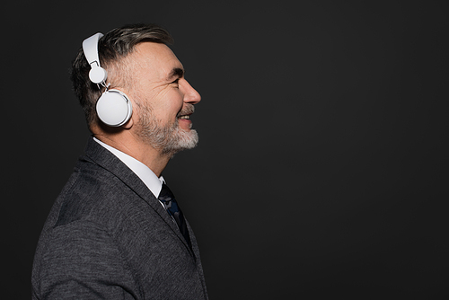 side view of cheerful bearded man listening music in headphones isolated on black
