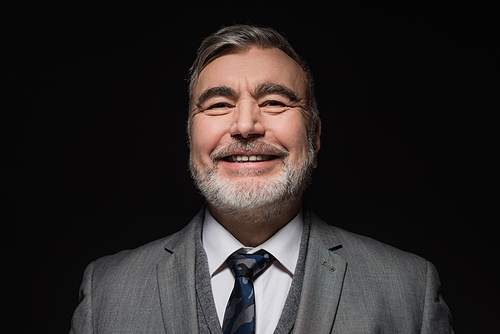 cheerful bearded man in formal wear smiling at camera isolated on black