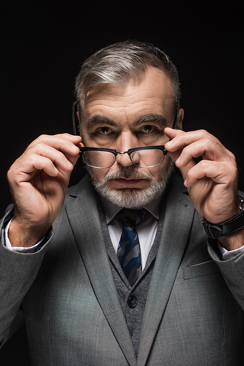 senior bearded businessman holding eyeglasses while  isolated on black