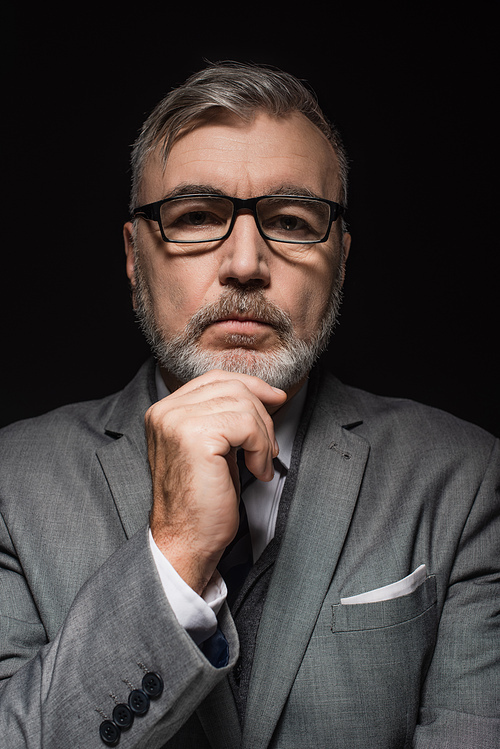 senior pensive businessman in eyeglasses touching chin while  isolated on black