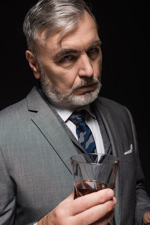 strict businessman in blazer and tie  near glass of whiskey isolated on black