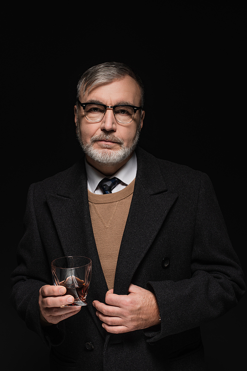 senior bearded man in coat and eyeglasses holding glass of whiskey isolated on black