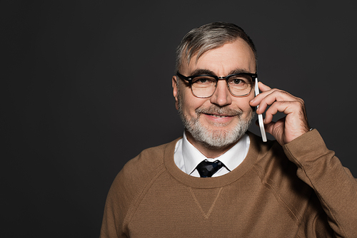 smiling man in beige jumper and eyeglasses talking on cellphone isolated on grey