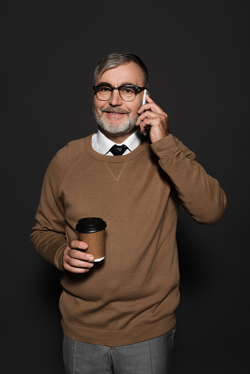 happy senior man with takeaway drink talking on mobile phone on dark grey