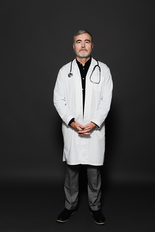 full length view of on senior physician in white coat  on dark grey