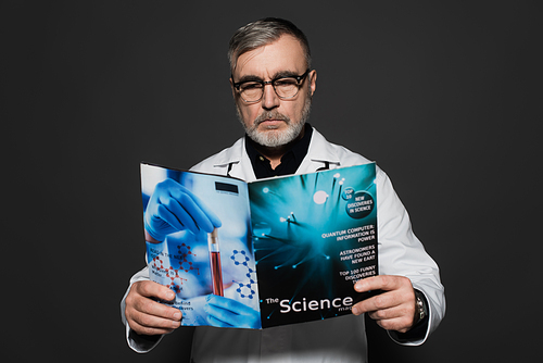 senior doctor in eyeglasses reading science magazine isolated on dark grey