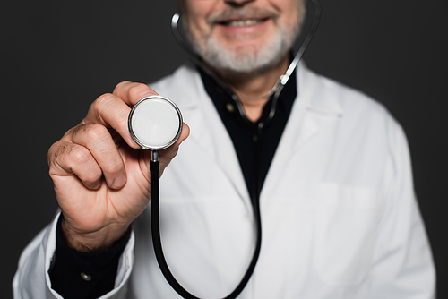 cropped view of blurred smiling physician holding stethoscope isolated on black