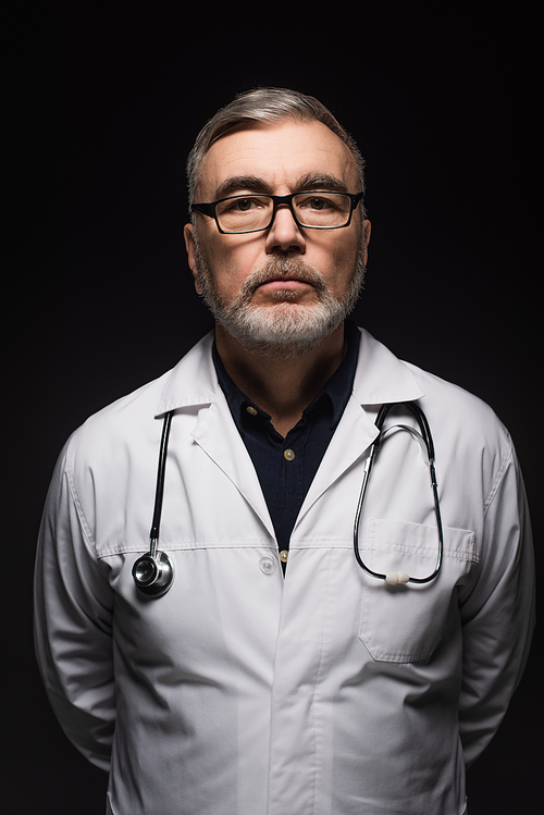 senior bearded doctor with stethoscope  isolated on black