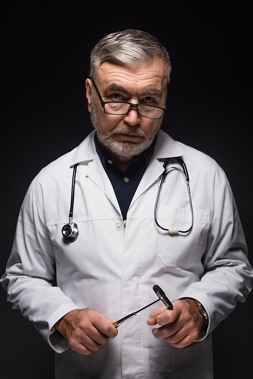 senior neurologist with reflex malleus and stethoscope  isolated on black