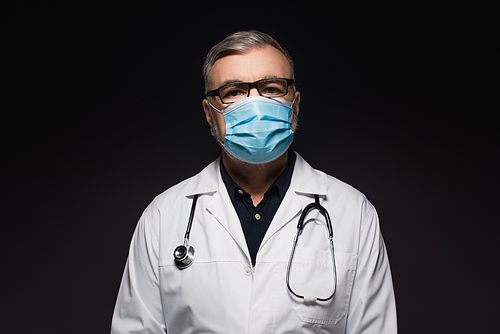 senior doctor in white coat and medical mask  isolated on black