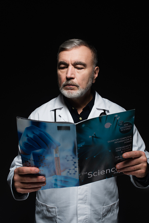 bearded physician in white coat reading science magazine isolated on black