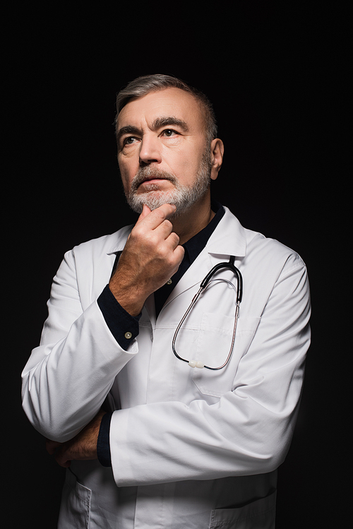 pensive doctor touching chin and looking away while thinking isolated on black