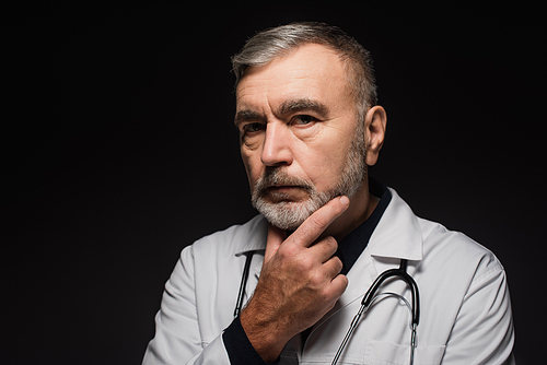 pensive bearded doctor  while touching chest isolated on black